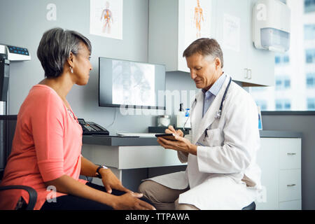 Male doctor writing prescription for female patient in clinic Stock Photo