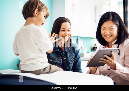 Happy doctor using tablet computer with family in clinic Stock Photo