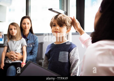 Doctor measuring boy's height while family sitting in clinic Stock Photo