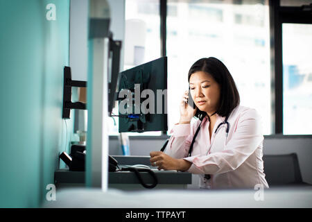 Female doctor using smart phone computer desk in clinic Stock Photo