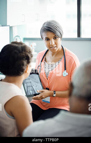 Female doctor explaining x-ray on tablet computer to family in clinic Stock Photo