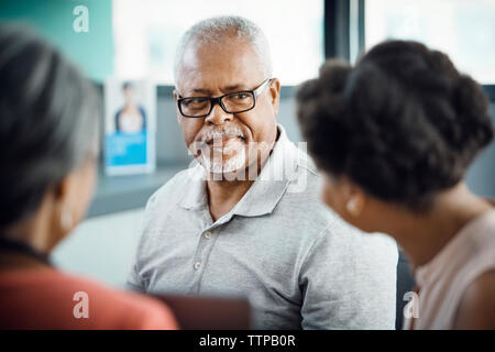 Senior male patient looking at daughter with female doctor in clinic