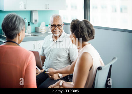 Smiling senior male patient sitting with daughter and female doctor in clinic Stock Photo
