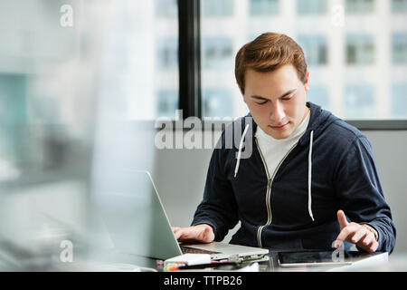 Male student using tablet computer while working on laptop at table in classroom Stock Photo