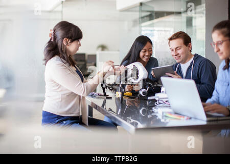 Female student repairing drone by friends using computer at table in classroom Stock Photo