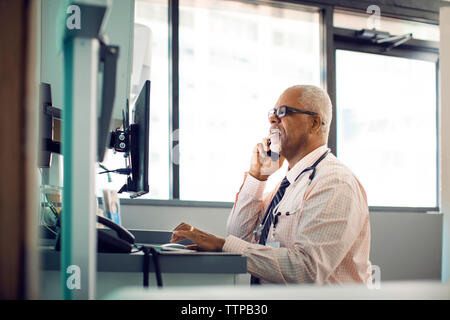 Doctor talking on mobile phone while using desktop computer in hospital Stock Photo