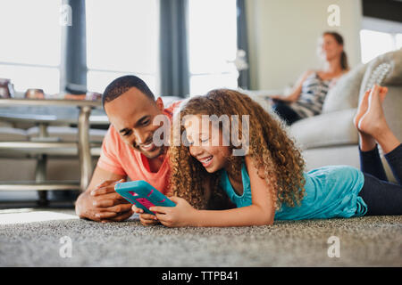 Happy father and daughter playing handheld game while lying on floor at home Stock Photo