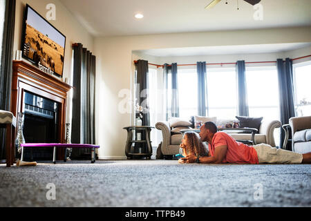 Father and daughter watching TV while lying on carpet at home