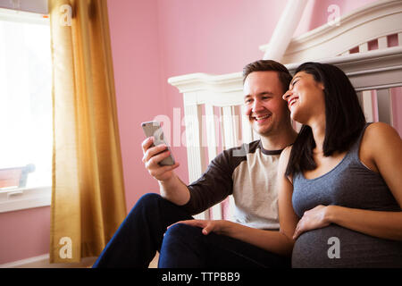 Happy man using smart phone while sitting by pregnant woman at home Stock Photo