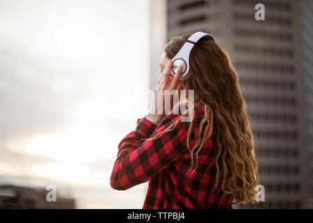 Side view of woman wearing headphones while standing against building Stock Photo