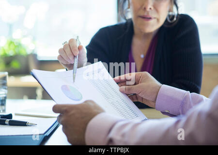 Cropped hands of businessman analyzing reports with colleagues in board room Stock Photo