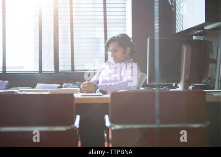 businessman using mobile phone in office seen through glass Stock Photo