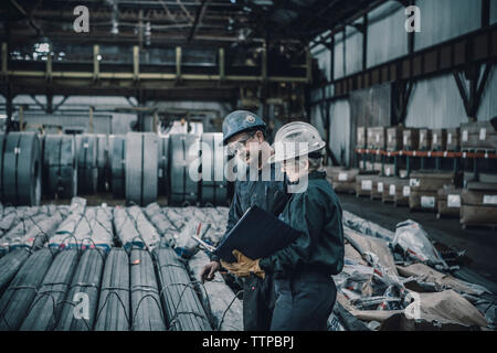 Coworkers discussing documents while walking in metal industry Stock Photo