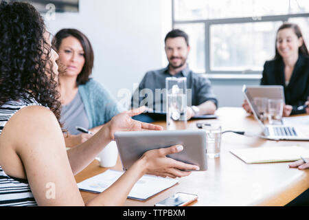 Young businesswoman explaining data from tablet computer to colleagues in meeting Stock Photo