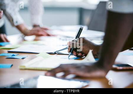 Cropped hands of businessman writing on sticky notes with colleague in board room Stock Photo