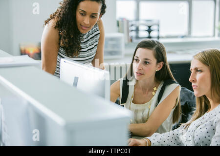 Female colleagues looking at desktop computer while working at desk in office Stock Photo