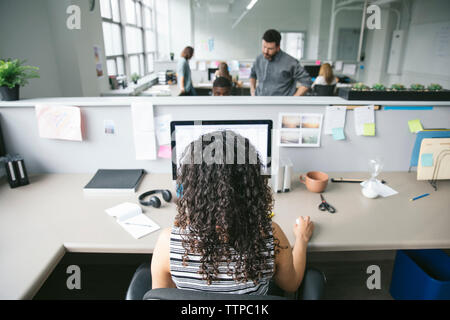 Rear view of businesswoman working on desktop computer with colleagues in background Stock Photo