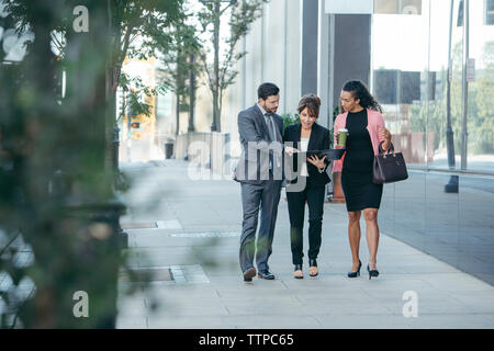 business people discussing over documents while walking on footpath Stock Photo
