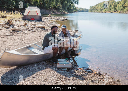 High angle view of friends talking while adjusting fishing tackles on boat at lakeshore Stock Photo