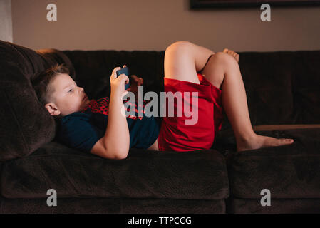 Boy using mobile phone while lying on sofa at home Stock Photo