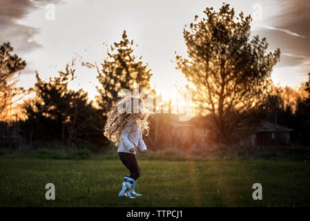 Girl with long curls jumping and playing in rain boots at sunset Stock Photo