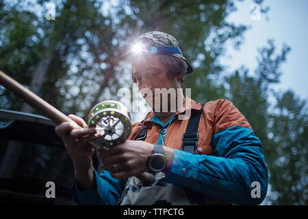 Low angle view of man holding fishing rod against trees Stock Photo