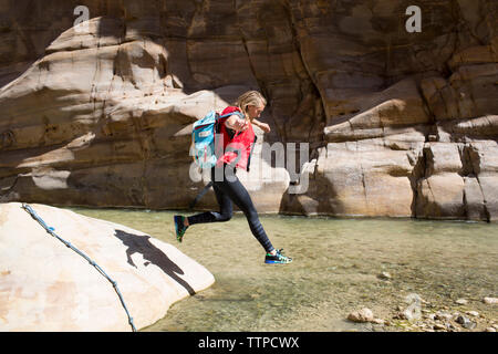 Female backpacker jumping in water on sunny day Stock Photo