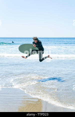 Man with surfboard jumping in sea against clear sky Stock Photo