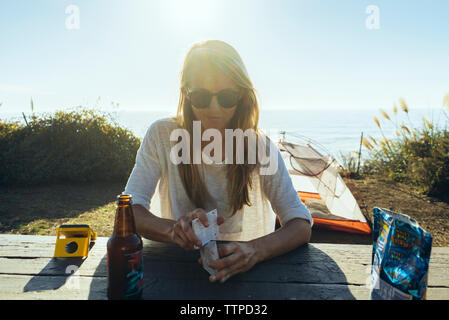 Woman holding cards while sitting at table on field against sea Stock Photo