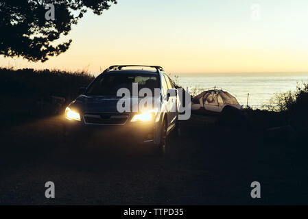 Car by tent on field against sea during sunset Stock Photo