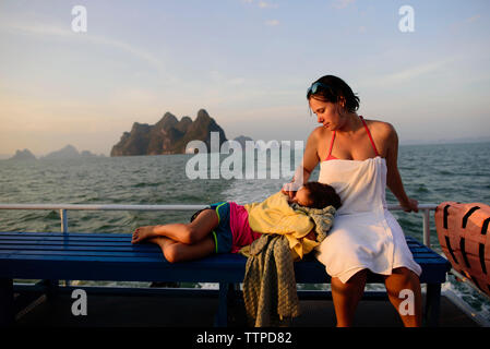 Mother looking at daughter sleeping on lap while traveling in boat Stock Photo