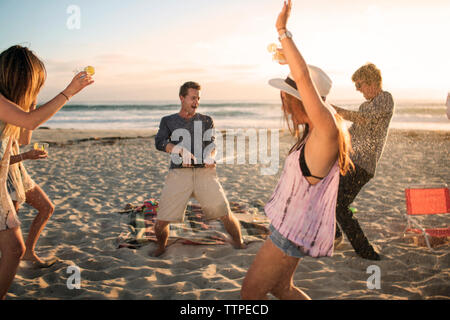 Happy man opening wine bottle while friends dancing on beach Stock Photo