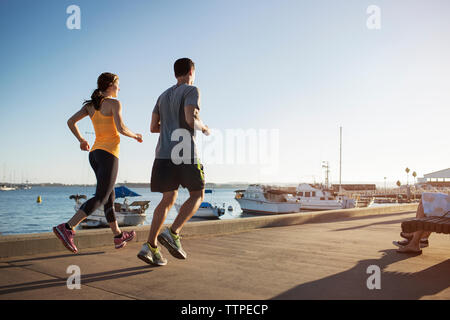 Rear view of male and female athletes jogging on pier by harbor Stock Photo