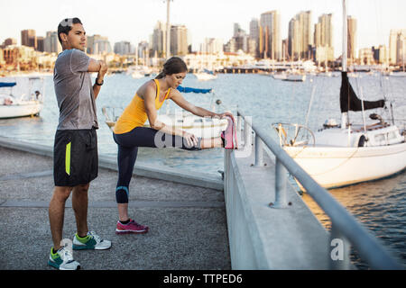 Male and female athletes doing stretching exercises on pier by harbor