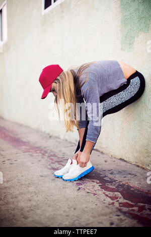 Sportswoman tying shoelace while standing on sidewalk Stock Photo