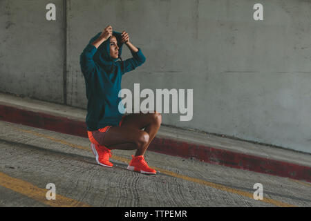 Woman putting on hood while crouching at road Stock Photo