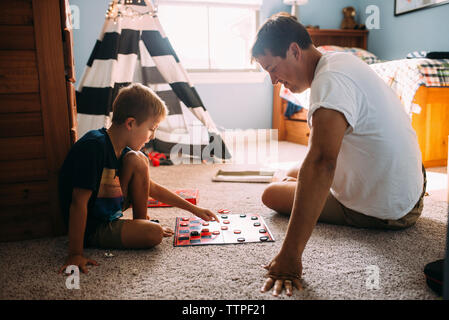 Father and son playing checkers while sitting on carpet at home Stock Photo