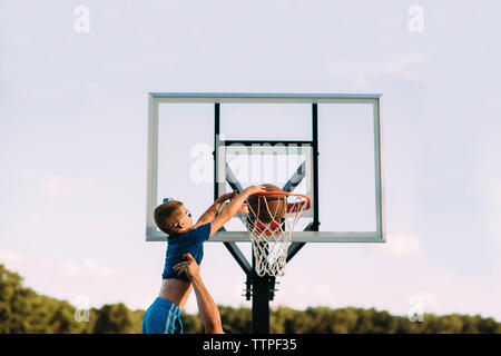 Cropped hand of father assisting son in taking basketball shot against sky Stock Photo