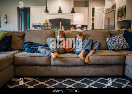 Brothers using tablet computers while relaxing on sofa at home Stock Photo