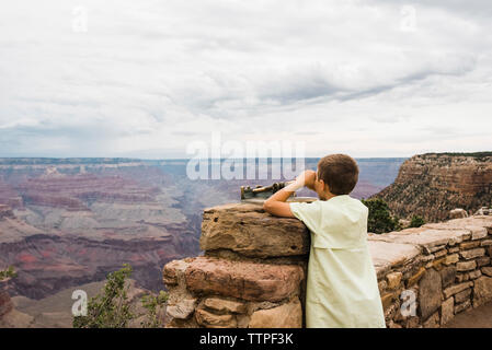 Rear view of boy looking through binoculars while standing in Grand Canyon National Park against cloudy sky Stock Photo