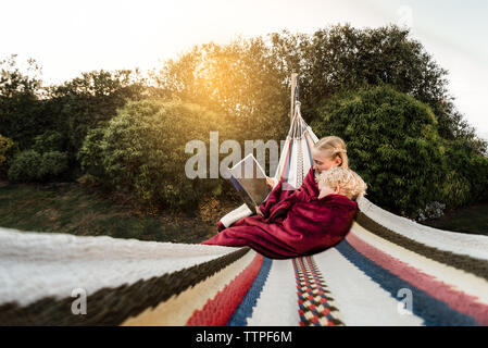 Older sister reading to younger brother in hammock outside Stock Photo
