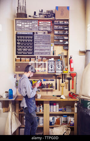 Craftsperson using phone while standing by tools at workshop Stock Photo