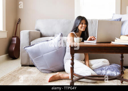Happy pregnant woman surfing internet on laptop at table in house Stock Photo