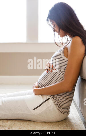 Side view of smiling pregnant woman sitting by sofa at home Stock Photo