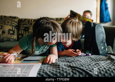 Siblings drawing while lying by father on bed at home Stock Photo