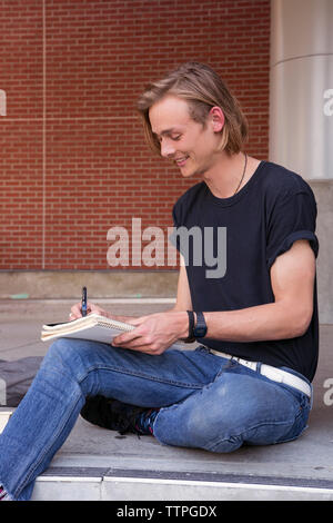 Male student smiling and writing on notebook Stock Photo