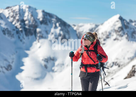 Thoughtful woman holding ski poles while standing against snowcapped mountains Stock Photo