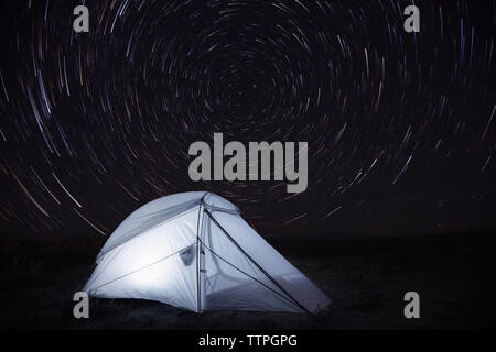 Illuminated tent on field against star trails Stock Photo