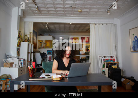 Female owner using laptop computer at table in gallery Stock Photo
