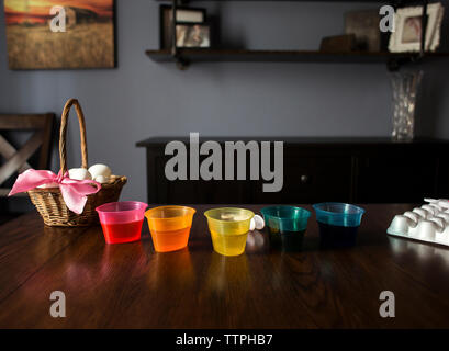 Dye in colorful bowls by eggs on wooden table at home during easter Stock Photo